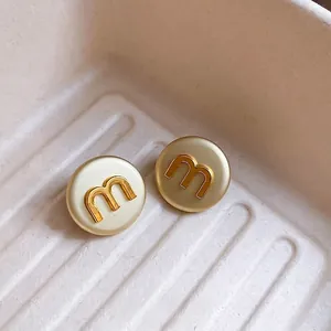 Minimalist round stud earrings with gold letter M and cream enamel on textured tray
