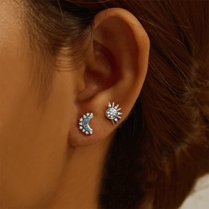 Close-up of asymmetrical sun and moon stud earrings with blue gems on model