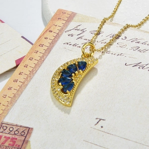 Detailed shot of a gold crescent moon pendant with blue and white zircon on an O-chain