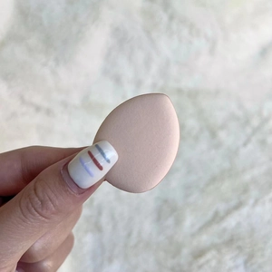 Close-up of a soft nude pink teardrop beauty sponge held to show elastic texture