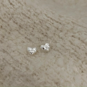 Close-up of heart-shaped silver earrings with bow relief on beige knit background