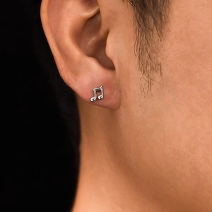 Macro shot of silver musical note stud earring worn on ear with high metallic luster