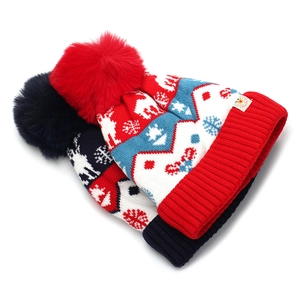Winter knit hats with reindeer and snowflake patterns featuring large faux fur pom-poms
