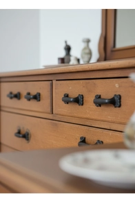 Detail of vintage black cast iron drawer handle mounted on a warm solid wood cabinet panel