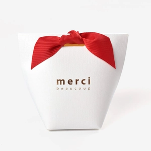 White gift box with red silk ribbon and gold merci beaucoup print on white background