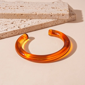 Macro detail of amber acrylic open bangle on natural stone with warm lighting