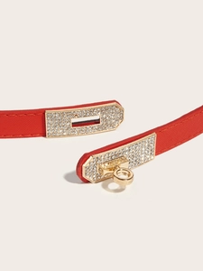 Close-up of red pebbled leather belt featuring a gold buckle with sparkling rhinestones