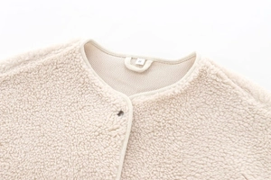 Close-up of beige teddy fleece jacket neckline with size S tag and soft woolly texture