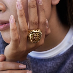 Détail d'une bague sphérique dorée à texture nid d'abeille portée par un mannequin