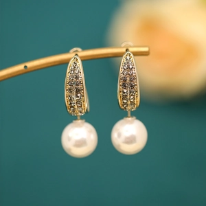 Detail shot of elegant gold pearl drop earrings with sparkling rhinestones on a gold stand