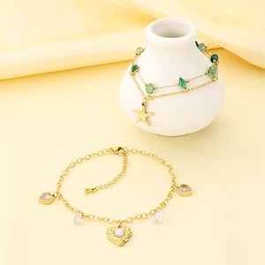 Detailed shot of golden layered anklets with starfish charms and green stones on silk