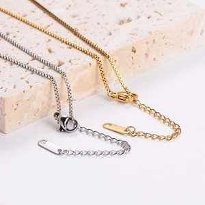 Detail of gold and silver box chains with lobster clasps on a textured stone surface