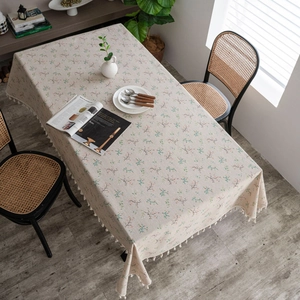 Close-up of beige cotton linen tablecloth with blue floral patterns and tassel edges