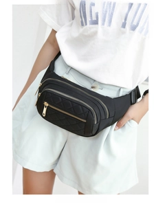 Detail view of black quilted waist bag with three zipper pockets and gold metal hardware