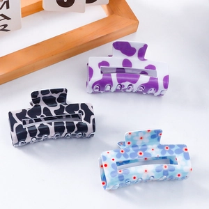 Three square PVC hair claws with cow print and floral patterns on white surface