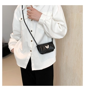 Close-up of black mini crossbody bag featuring a gold butterfly buckle on model