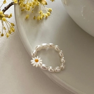 Baroque pearl ring with daisy floral charm on a ceramic dish under soft natural light