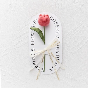 Close-up of a handmade pink crochet tulip with ribbon and elegant gift card packaging
