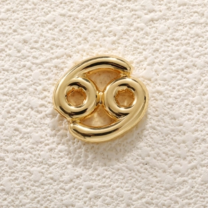 Macro shot of gold-plated Cancer zodiac pendant on a textured beige surface
