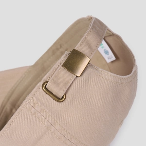 Close-up of adjustable bronze metal buckle on beige cotton twill baseball cap back