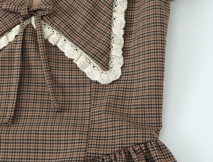 Detail of oversized collar with white lace trim and bow on brown plaid dress
