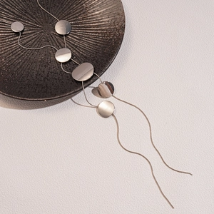 Minimalist long silver tassel necklace featuring circular polished metallic discs on a sleek chain