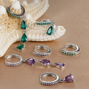 Macro detail of silver drop earrings with green and purple zircons on white starfish