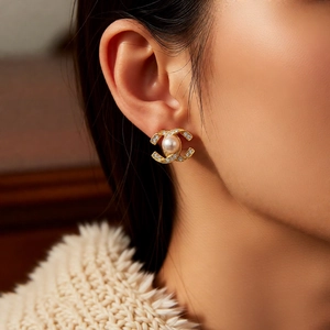 Close-up of 14k gold plated double-C pearl earrings worn by a model in a warm setting