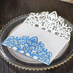 Macro detail of laser-cut wedding invitation with white floral pattern and blue glitter