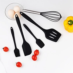 Set di 5 utensili da cucina in silicone nero con frusta, spatole e pennello su sfondo bianco