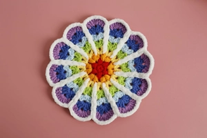 Detailed top view of rainbow hand-knitted flower coaster with white scalloped edge trim