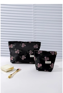 Detail of two-piece black satin makeup bag set with rose embroidery and gold flower zippers