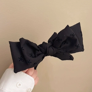 Detail showing hand holding black fabric bow hair clip with fine embroidery patterns