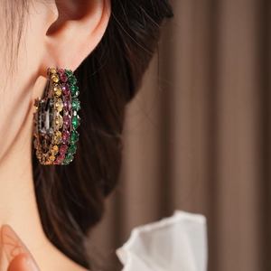 Close-up of vintage hoop earrings with green and purple zircons on model ear