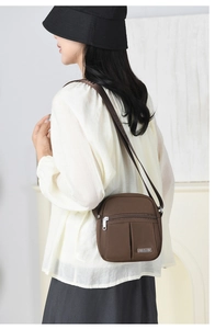 Brown nylon crossbody bag with dual front zippers and adjustable shoulder strap worn by model