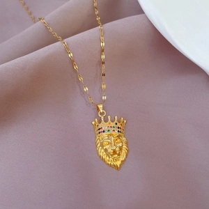 Detailed close-up of golden lion head pendant with crystal crown on pink fabric background