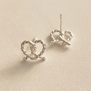 Close-up of silver twist knot heart stud earrings on a textured minimalist background