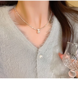 Detail of silver pearl necklace with zircon pendant worn on a cozy sweater