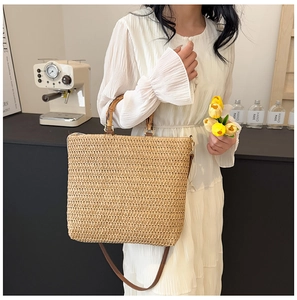 Detail of the woven straw bag featuring a bamboo top handle and brown shoulder strap