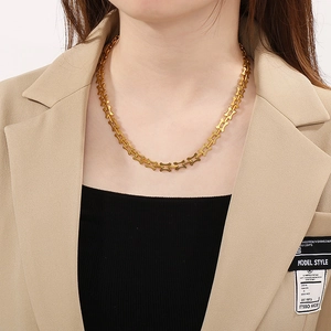 Close-up of gold bone-shaped link necklace worn by a model in a stylish beige blazer
