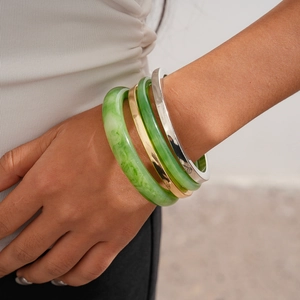 Details der gestapelten grünen Harz- und Gold-Silber-Metallarmbänder an einem Handgelenk