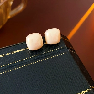 Close-up of square cream pearl earrings on a luxury navy blue textured jewelry gift box