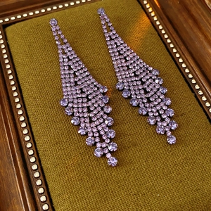Vue macro de boucles d'oreilles pompon en strass violet dans un écrin en velours vert