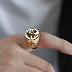 Close-up of golden stainless steel signet ring with compass design worn on finger