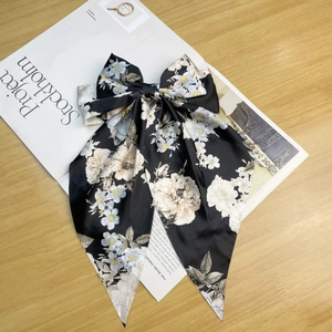 Detail of floral black satin hair clip with long ribbons on a minimalist magazine background