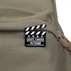 Detailed close-up of a movie clapperboard enamel pin on olive green fabric material