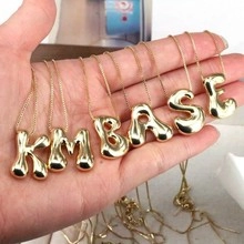 Detailed view of 3D gold bubble letter pendant necklace held in hand to show scale