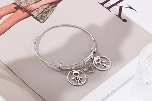 Detail of silver stainless steel cuff bracelet with boy, heart, and girl charms