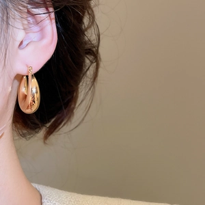 Gros plan d'une large créole en or poli au fini miroir minimaliste sur l'oreille de la femme