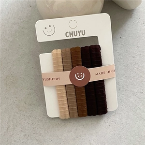 Detail of five earth-toned ribbed hair ties on a white card display with warm color gradient